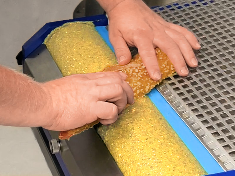 Hände führen eine Brötchenhälfte mit der Schnittfläche über die benetzte Auftragswalze des spreadROLL 400